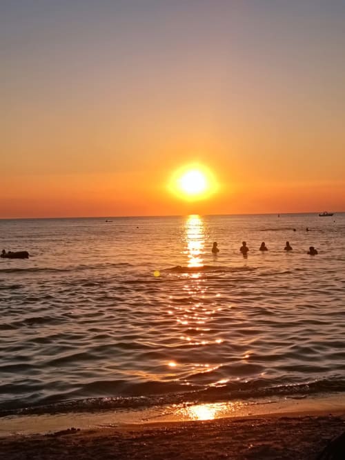 Tramonto sulla spiaggia di Lido Conchiglie a Gallipoli con bagnanti nelle acque dorate dell'ora magica vicino a Le Case di Esteca