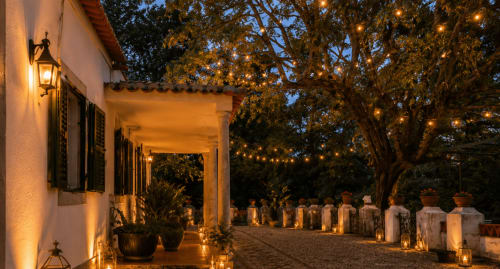 Pátio da Quinta Do Carril ao entardecer, iluminado por lanternas acesas sob árvores centenárias, Portugal