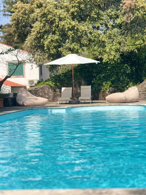Piscina da Quinta do Carril com espreguiçadeiras, sombrinha branca e jardim exuberante em Portugal