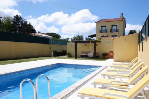 Blue rectangular pool with yellow lounge chairs at Be SilverCoast hotel in Serra D'El Rei, Portugal, featuring yellow villa