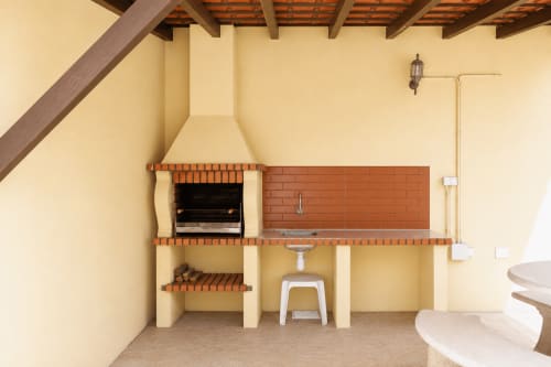 Outdoor barbecue and kitchenette area at Be SilverCoast villa with brick grill, sink, and wooden ceiling beams