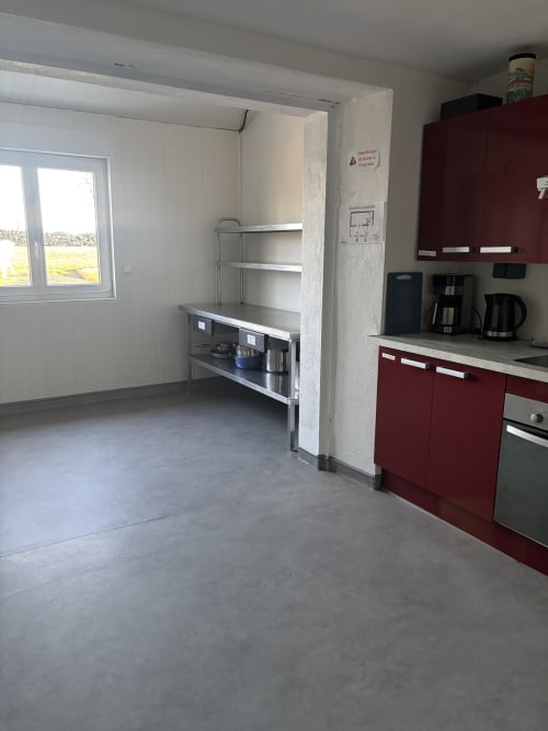 Cuisine cottage moderne avec armoires bordeaux, appareils inox et sol en béton au Mas De Bannayoux