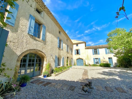 La cour du Mas de la Soie à Violes, France avec ses bâtiments en pierre, volets bleus et patio ensoleillé