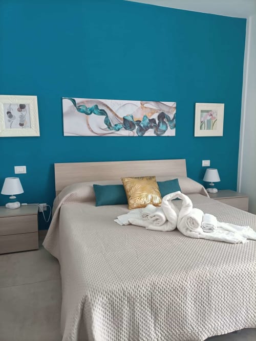 Camera da letto moderna blu presso Le Case di Esteca con parete turchese, arte botanica e asciugamani bianchi arrotolati al Lido