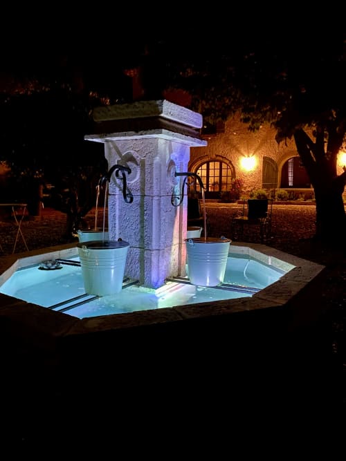 Fontaine-puits illuminée du Mas de la Soie à Violes, France, éclairée en bleu la nuit avec seaux