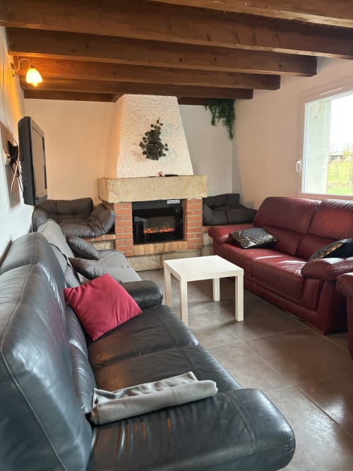 Salon cosy du Mas De Bannayoux avec cheminée, poutres apparentes, canapés cuir et vue montagne à Couteuges