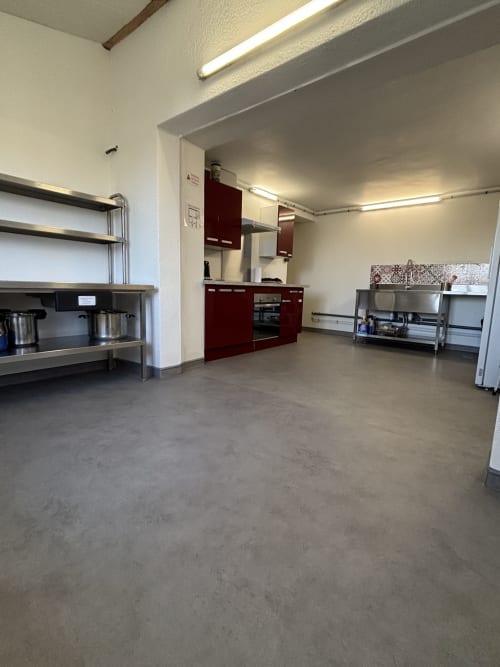 Spacieuse cuisine-réception au Mas De Bannayoux avec armoires bordeaux, plan de travail inox et sol béton