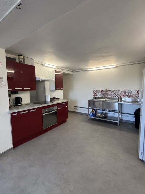 Cuisine professionnelle de la salle de réception Mas De Bannayoux avec mobilier rouge, plan de travail inox et équipements professionnels