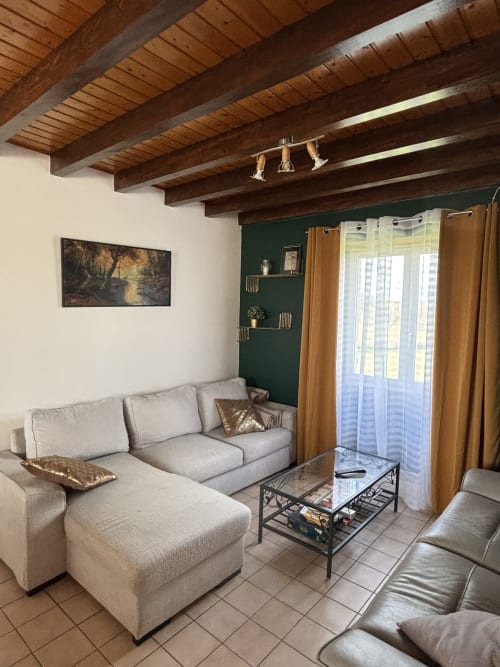 Salon chaleureux du Mas De Bannayoux avec canapé sectionnel beige, poutres en bois, mur accentué vert foncé et vues sur les montagnes