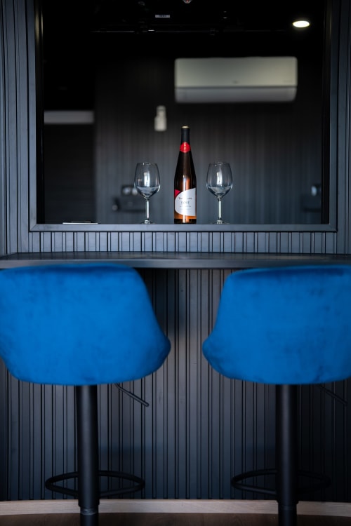 Angolo bar moderno con bottiglia di vino, bicchieri e sgabelli blu nell'appartamento BHE House Boat Experience a Cesena
