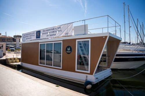 Esperienza BHE House Boat ormeggiata in marina a Cesena con design moderno di house boat marrone e bianco e barche a vela