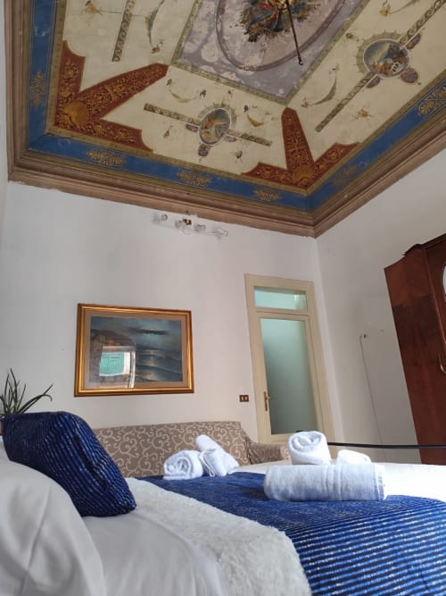 Camera Blu presso Mappamondi B&B Venezia con soffitto affrescato ornato, letto a righe blu con asciugamani arrotolati, e