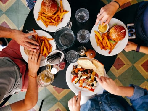 Vue de dessus de convives partageant burgers, frites et boissons aux Troglos de Beaulieu, gîte français