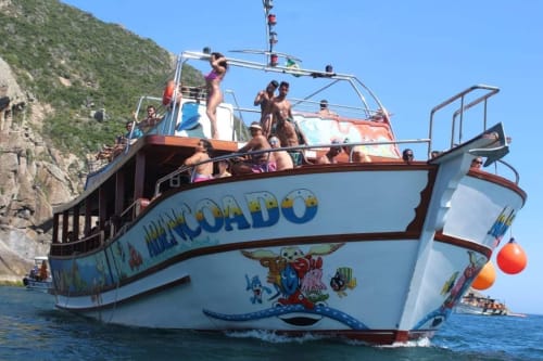 Barco de passeios colorido 'Mancordo' repleto de turistas na costa do Rio de Janeiro, oferecendo atividades aquáticas perto do Rio Vibes Hostel