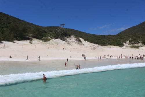 Águas turquesas e praia de areia branca com visitantes nadando e relaxando perto das dunas, Rio de Janeiro