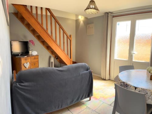 Séjour ouvert du gîte Suzon avec canapé sombre, escalier en bois, TV, table à manger et vue sur le jardin