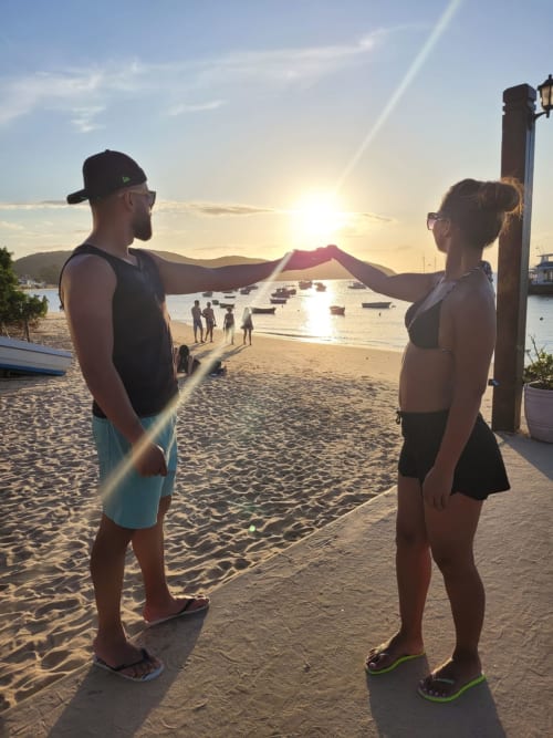 Dois hóspedes segurando tecido ao pôr do sol na praia perto do Rio Vibes Hostel no Rio de Janeiro com barcos e montanhas
