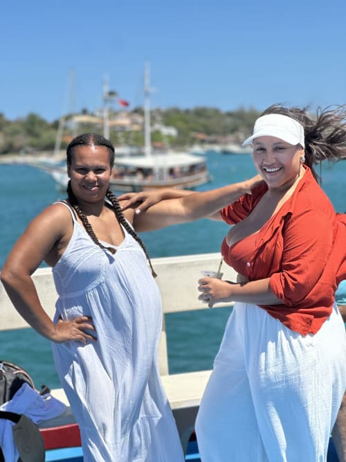 Duas mulheres sorrindo no hostel Rio Vibes à beira-mar no Rio de Janeiro, com veleiros e baía turquesa ao fundo
