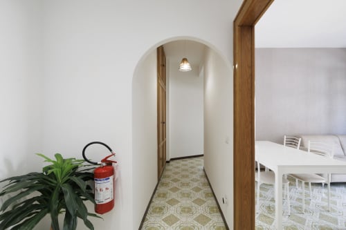 Ingresso del corridoio dell'appartamento ViOletta Roma con porta ad arco, estintore rosso, pianta e area pranzo bianca visibili
