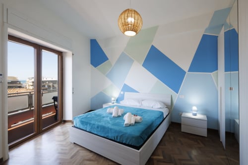 Camera da letto moderna con arte geometrica blu, balcone con vista mare e arredi contemporanei a ViOletta Roma