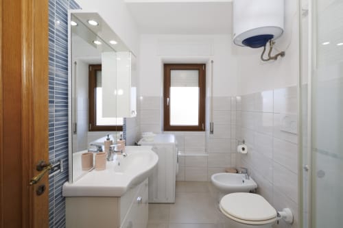 Bagno moderno nell'appartamento Profumo di Mare con vista sul mare dell'hotel ViOletta a Roma, con piastrelle bianche, doppio lavabo e WC