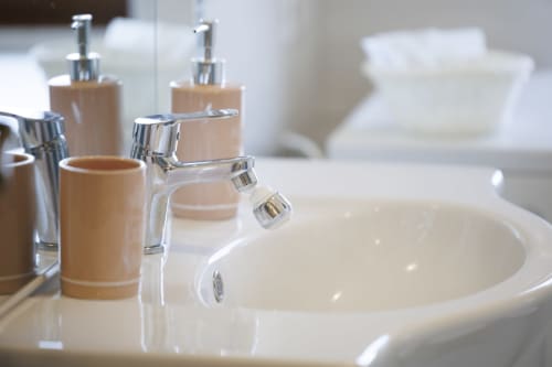 Moderno lavabo del bagno con lavello bianco rotondo, dispenser di sapone in legno e rubinetto cromato nell'appartamento ViOletta Roma