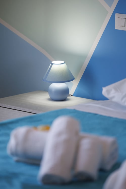 Moderna lampada da comodino con paralume conico in luminoso appartamento con vista mare a ViOletta Roma, pareti blu e morbida biancheria