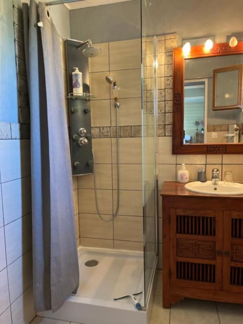 Salle de bain moderne avec douche vitrée, murs en carrelage beige, vasque en bois et miroir rétroéclairé aux Chambres Et Gîte