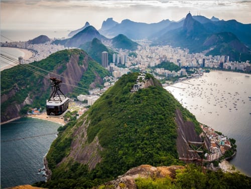 Vista aérea do Rio de Janeiro mostrando o Pão de Açúcar, bondinho, baía com barcos e picos icônicos da pousada Rio Vibes