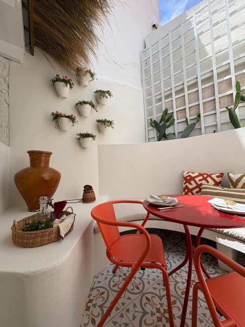Pátio aconchegante da Casa Amanhada com mesa bistro vermelha, flores em vasos e vista para a cidade em Grândola