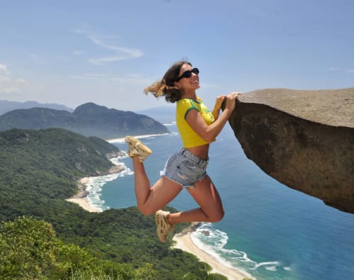 Mulher pulando à beira de um penhasco com vista para o litoral tropical perto do Rio de Janeiro, Brasil na Rio Vibes Hostel