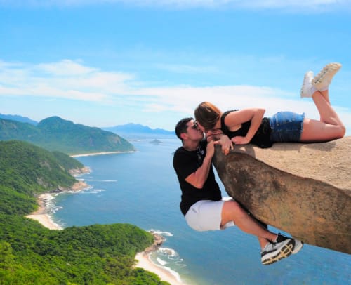 Casal se beijando à beira de um penhasco com vista para a costa do Rio de Janeiro, montanhas e praias