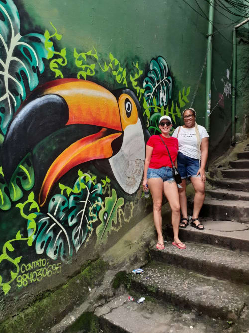 Dois hóspedes posando diante de uma colorida arte de rua com tucano no Rio Vibes Hostel no Rio de Janeiro