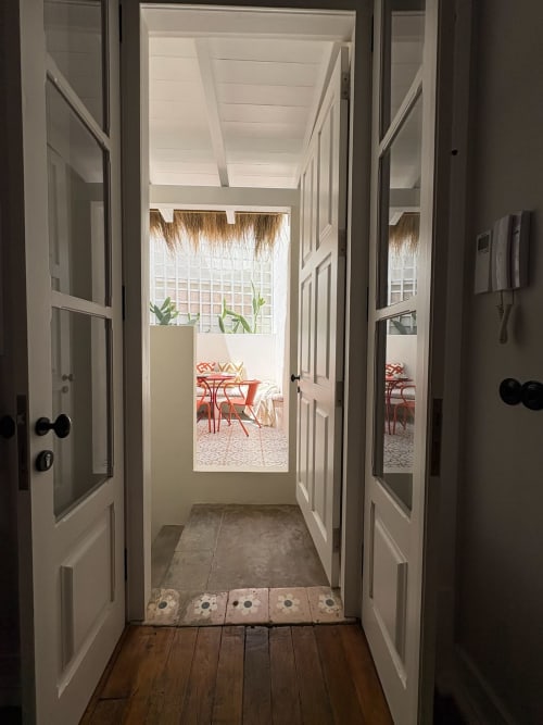 Portas duplas abertas revelando varanda ensolarada com cadeiras vermelhas na Casa Amanhada, Grândola