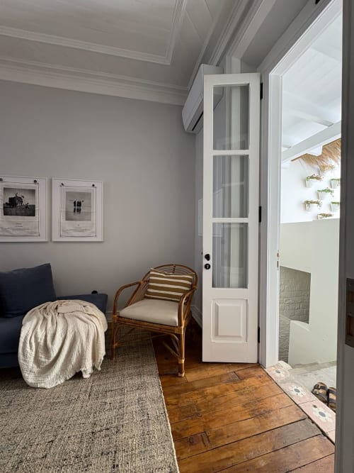 Quarto luminoso na Casa Amanhada com cadeira de ratã, almofada listrada, assoalho de madeira e porta aberta para o pátio em Grândola