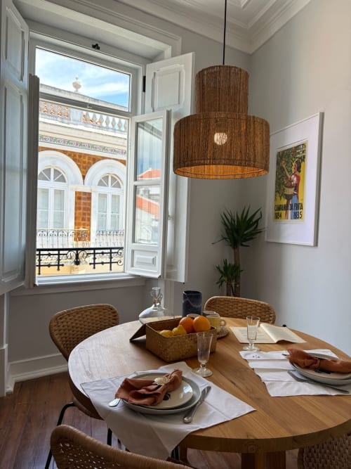 Sala de jantar elegante na Casa Amanhada em Grândola com mesa redonda de madeira, luminária de vime e vistas da cidade através de vidraças