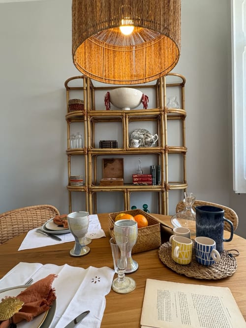Pousada de mesa para refeição na Casa Amanhada com prateleiras em rattan e luminária tejida ao fundo em Grândola