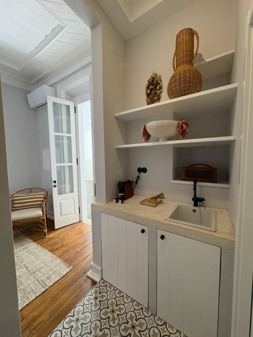 Kitchenette do apartamento Casa Fataca com armários brancos, pia, cestos de vime e prateleiras flutuantes em Grândola, Portugal