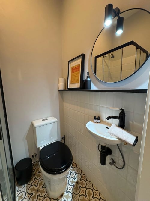Casa Amanhada: banheiro moderno com vaso preto, pia branca, espelho redondo e azulejos decorativos em Grândola