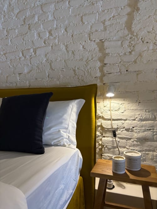Quarto moderno da Casa Amanhada em Grândola com cabeceira mostarda, roupa de cama branca, parede de tijolos à vista e mesa de cabeceira em madeira