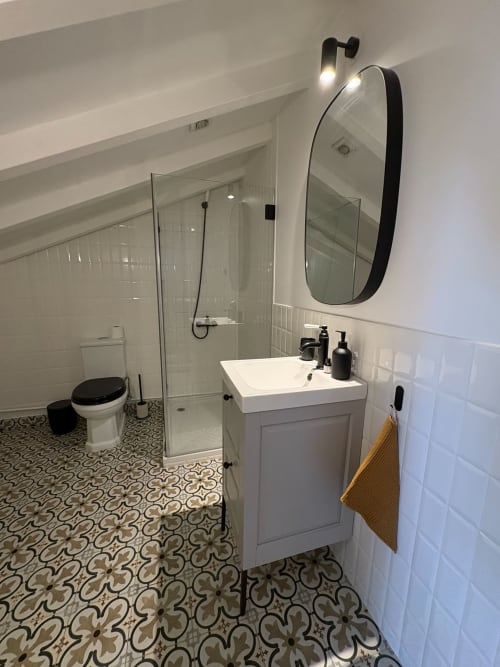 Banheiro moderno da Casa Amanhada em Grândola com pia branca, espelho oval, chuveiro amplo e piso com azulejos estampados.