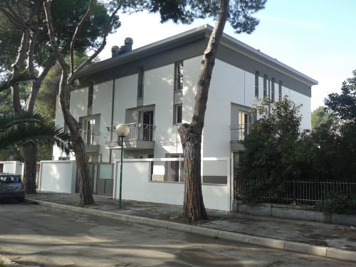 Modern white apartment building at Pescara INN Pineta Retreat with garden view, tree-lined street, accessible design, Pescara