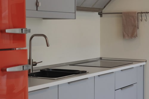 Modern kitchenette in Pescara INN apartment with red cabinetry, stainless steel sink, and white countertops