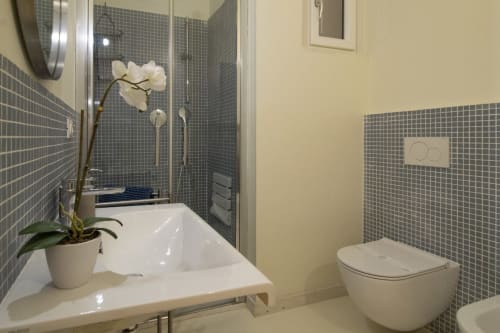 Modern bathroom at Pescara INN Pineta Retreat with gray tiled shower, white sink, toilet, and white orchid plant