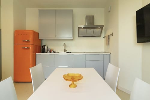Modern kitchen and dining area at Pescara INN with orange retro fridge, white chairs, and amber glass decor