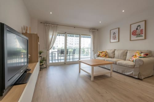 Luminosa sala de estar moderna en Wellhome Alicante con sofá beige, muebles de madera, TV y balcón con vistas a la ciudad