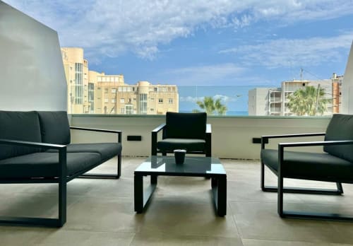 Terraza moderna en la azotea de Wellhome Alicante con tumbonas negras, vista al mar y arquitectura costera mediterránea