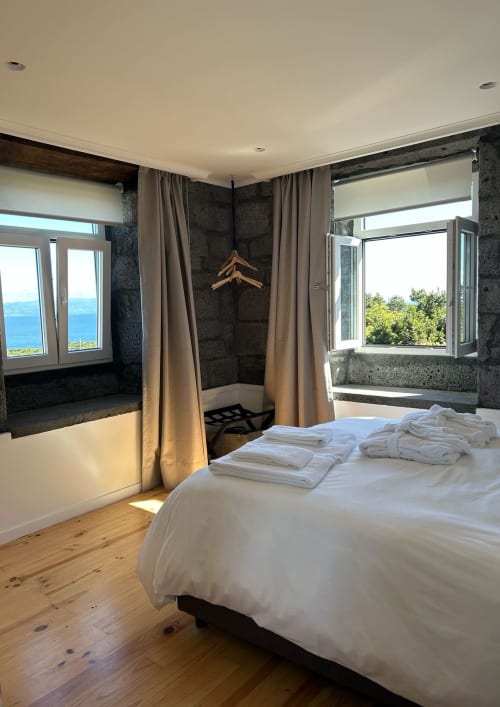 Quarto moderno em Cá Por Casa Pico com vista para o mar, pisos em madeira, paredes de pedra escura e móveis contemporâneos nos Açores