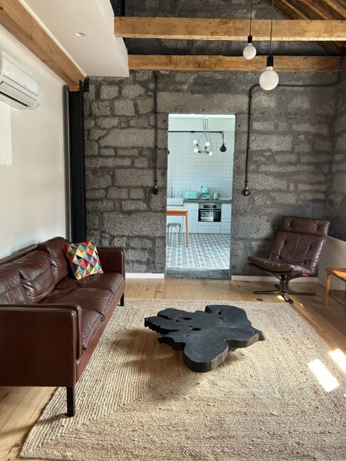 Sala de estar moderna com mobiliário em couro, paredes de pedra aparente, vigas de madeira e cozinha aberta em Cá Por Casa Pico Açores