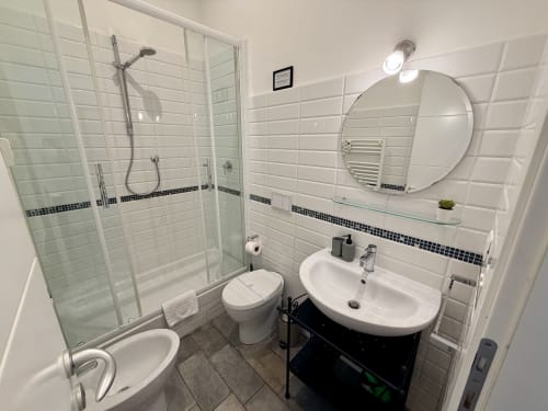 Bagno moderno presso Enjoy Vatican B&B a Roma con piastrelle bianche, doccia in vetro, specchio rotondo e finiture scure